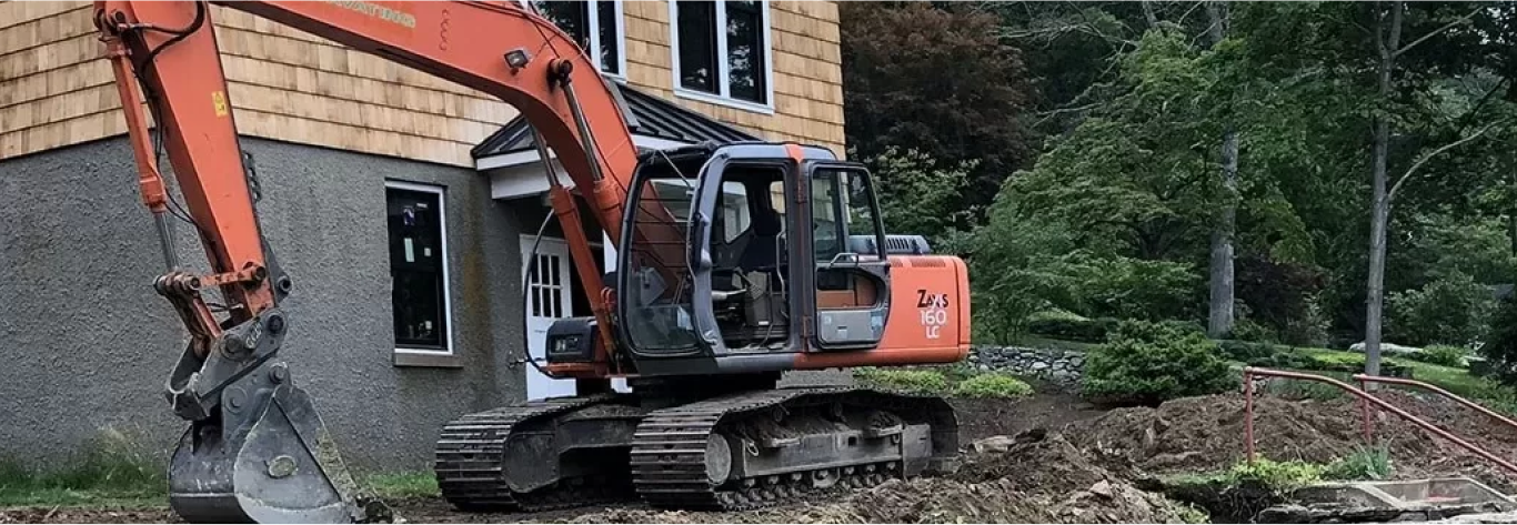 Orange excavation machine right next to a new construction house digging up dirt by Cranehill Contracting